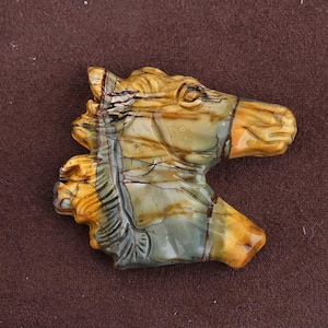 May include: A carved stone horse head sculpture. The sculpture features a detailed design with a mix of colors, including tan, brown, and green. The horse head is a decorative item.