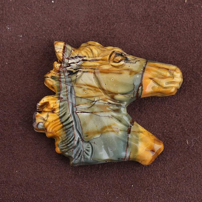 May include: A carved stone horse head sculpture. The sculpture features a detailed design with a mix of colors, including tan, brown, and green. The horse head is a decorative item.