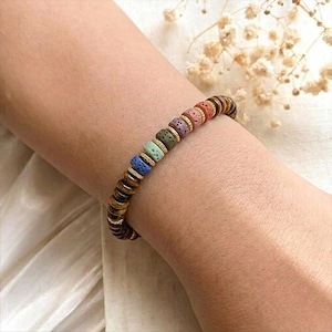 May include: A beaded bracelet featuring a variety of colorful beads, including blue, green, purple, pink, and brown. The bracelet is accented with gold-colored spacers and has a natural, earthy aesthetic. The bracelet is worn on a wrist.