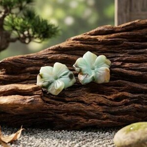 May include: Two light green flower-shaped objects with a marbled appearance rest on a piece of dark brown wood. The flowers have multiple petals and a natural, organic aesthetic. The background is blurred, suggesting an outdoor setting.