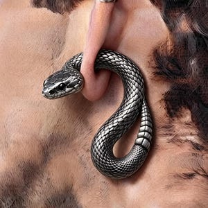 以下が含まれることがあります： 耳たぶを通るようにデザインされた、銀色のヘビ型イヤーゲージ。細かな鱗の質感が施された湾曲した胴体が特徴で、ヘビの頭部が前方を向き、尾が下に向かってカーブを描きながら円形のシルエットを形成しています。