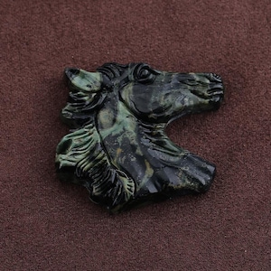 May include: A carved horse head sculpture in shades of green and black. The sculpture is detailed, with a focus on the horse's mane and facial features. The artwork is set against a brown background.