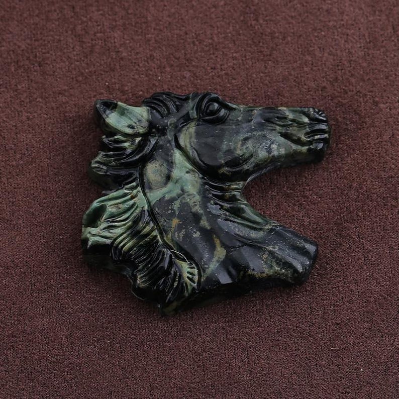 May include: A carved horse head sculpture in shades of green and black. The sculpture is detailed, with a focus on the horse's mane and facial features. The artwork is set against a brown background.