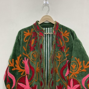 K&ouml;nnte beinhalten: Gr&uuml;ne Samtjacke mit aufwendiger Blumenstickerei in Orange, Rot und Rosa. Die Jacke hat einen Stehkragen und ein gestreiftes Futter. Die Stickerei ist detailliert und bedeckt Vorder- und &Auml;rmel.