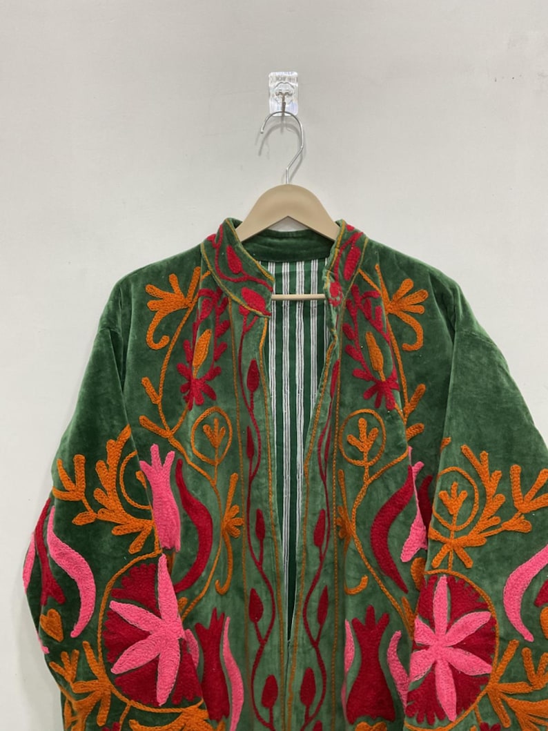 K&ouml;nnte beinhalten: Gr&uuml;ne Samtjacke mit aufwendiger Blumenstickerei in Orange, Rot und Rosa. Die Jacke hat einen Stehkragen und ein gestreiftes Futter. Die Stickerei ist detailliert und bedeckt Vorder- und &Auml;rmel.