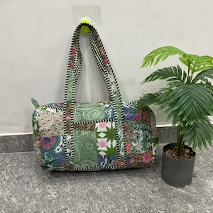 May include: A patchwork duffel bag with floral and paisley patterns in shades of green, pink, and blue. The bag has two handles and a zip closure. The bag is on a grey tiled floor.