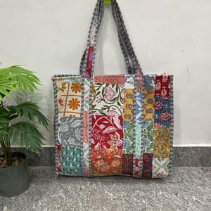 Può includere: Una borsa tote patchwork con una varietà di motivi floreali e geometrici nei toni del rosso, arancione, giallo, blu e verde. La borsa ha una forma rettangolare con manico e finiture a righe.