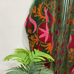 K&ouml;nnte beinhalten: Nahaufnahme eines gr&uuml;nen Samtgewands mit aufwendiger Stickerei. Die Stickerei zeigt ein Blumenmuster in Rot-, Orange- und Rosat&ouml;nen. Das Kleidungsst&uuml;ck hat ein gestreiftes Futter und eine lockere Passform.