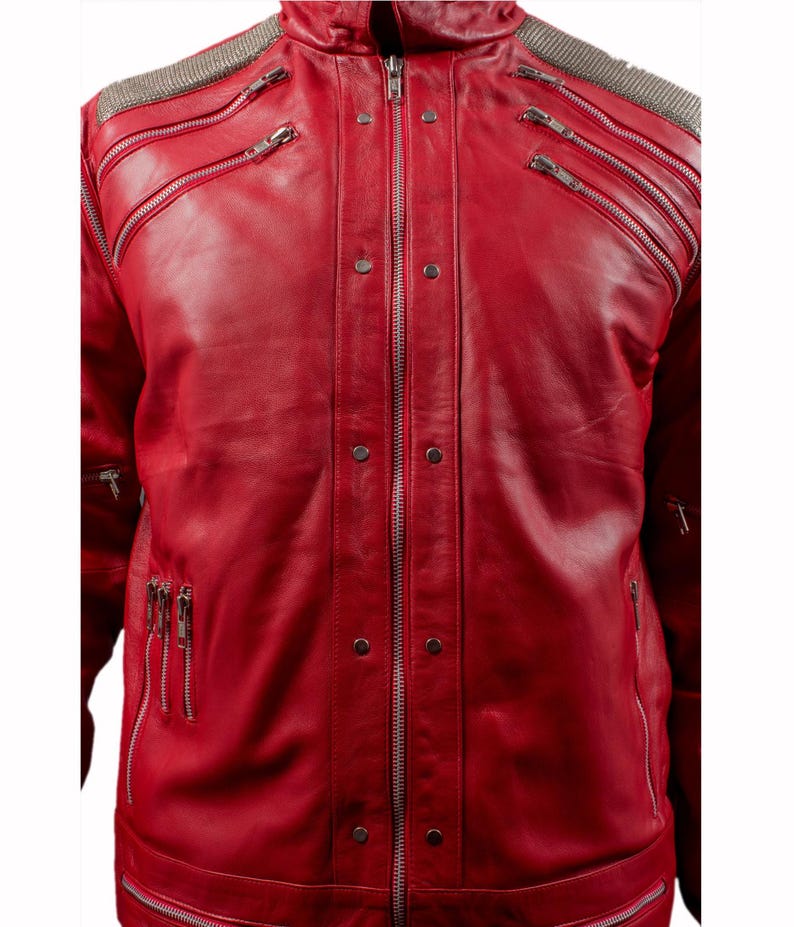 Pode incluir: Jaqueta de couro vermelho vibrante com m&uacute;ltiplos z&iacute;peres prateados e detalhes de ombro com tachas prateadas. A jaqueta tem gola alta e corte sob medida, com v&aacute;rios bolsos com z&iacute;per e costuras decorativas.