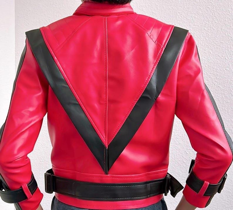 May include: A red leather jacket with black accents. The jacket features a black V-shaped design on the back and black stripes on the sleeves. It has a black belt at the waist and black cuffs. The jacket is a vibrant red color.