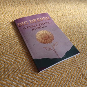 Op de afbeelding: Een softcover journal met een paarse gradiënt omslag met de tekst DIG DEEPER WEEKLY RITUAL JOURNAL in gouden letters. Een gedetailleerde illustratie van een zonnebloem staat centraal op de omslag boven een donkere, textuurrijke afbeelding.