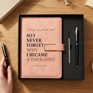 Op de afbeelding: Een perzikkleurig notitieboek met een goudkleurige metalen sluiting, voorzien van de tekst "Things my patients said SO I NEVER FORGET WHY I BECAME A THERAPIST" en "EMMA COLLINS" in het zwart, gepresenteerd in een zwarte doos met pen en vulling.