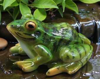 Könnte beinhalten: Detaillierte grüne Froschfigur mit schwarzen Streifen und gelben Akzenten. Der Frosch ist in einer entspannten Position mit offenen Augen dargestellt. Die Figur ist wahrscheinlich aus Kunstharz oder einem ähnlichen Material und für die Dekoration geeignet.