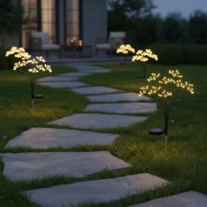Può includere: Luci da giardino a energia solare. Hanno uno stelo nero e un gruppo di piccole luci a LED bianco caldo che assomigliano a fuochi d'artificio o fiori. Sono posizionate lungo un sentiero di pietra in un giardino.