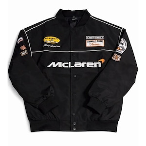 May include: Black McLaren racing jacket with white detailing and several embroidered patches. Features the McLaren logo across the chest and racing team emblems. It has a button-up front and a classic bomber jacket design.