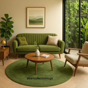 Puede incluir: Un salón con un sofá verde, una mesa de centro redonda de madera y una alfombra verde circular. Una pintura de paisaje cuelga sobre el sofá. También se ve una mesa auxiliar con una lámpara y una planta en maceta.