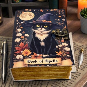 May include: A decorative journal titled "Book of Spells" features a black cat wearing a witch hat, set against a starry night sky with a full moon. The journal has a clasp closure and aged-looking pages.
