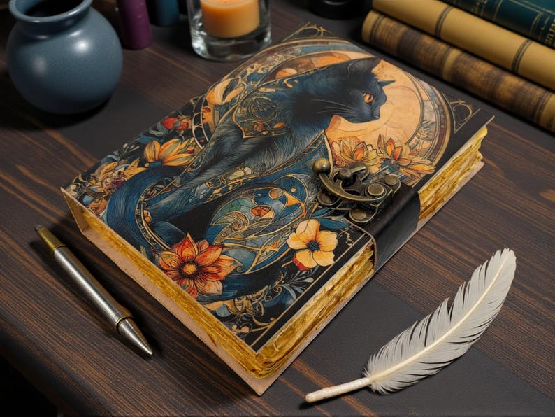 May include: A decorative journal with a black cat illustration on the cover, featuring orange and yellow flowers and a brass clasp. A silver pen and a white feather are placed nearby. The journal's pages have a vintage, aged appearance.