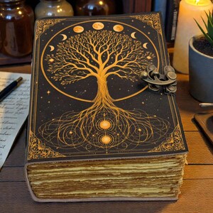 May include: A detailed journal with a tree of life design on the cover. The cover is black with gold accents, a metal clasp, and a celestial design. The pages are aged, and the journal is open, revealing the textured paper.
