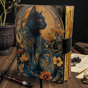 May include: A decorative journal with a black cat illustration. The cover features a detailed design with a black cat, flowers, and ornate patterns in shades of blue, gold, and orange. The journal has a leather strap closure and aged-looking pages.