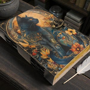 May include: A decorative journal with a black cat illustration on the cover, surrounded by floral and celestial designs. The journal has a metal clasp and gold-edged pages. A white feather quill rests beside it on a dark wooden surface.