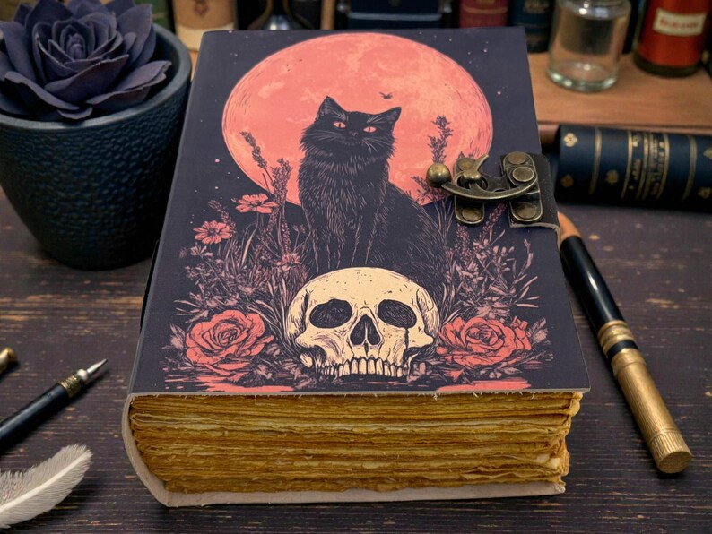 K&ouml;nnte beinhalten: Dekoratives Notizbuch mit einer Illustration einer schwarzen Katze, einem Totenkopf und Rosen vor einem roten Mond. Das Notizbuch hat einen Metallverschluss und gealterte Seiten. Das Cover ist dunkel mit Vintage-&Auml;sthetik.