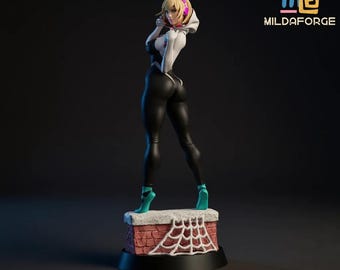 May include: A figurine of a female superhero in a black and white suit, standing on a brick base with a spiderweb design. The figure has blonde hair and is wearing teal heels. The logo "MILDAFORGE" is visible.