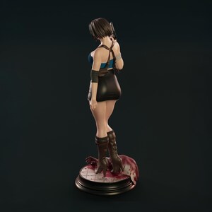 May include: A detailed figurine of a woman in a blue top, black skirt, and brown boots, holding a gun. The figure is posed on a circular base with a bloody scene. The color scheme is dark, highlighting the character's outfit and stance.