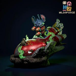 Peut inclure: Figurine détaillée d'un personnage extraterrestre bleu chevauchant un véhicule rouge et vert en forme de fusée. Le personnage porte une tenue rouge et marron. La base est une formation rocheuse gris foncé avec des accents verts. Le logo "MILDAFORGE" est visible.