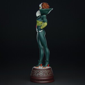 Pode incluir: Estatueta verde de um personagem com rosto branco e amarelo, cabelo ruivo e roupa verde. O personagem est&aacute; usando botas verdes com saltos laranja e est&aacute; em p&eacute; em um pedestal decorativo.