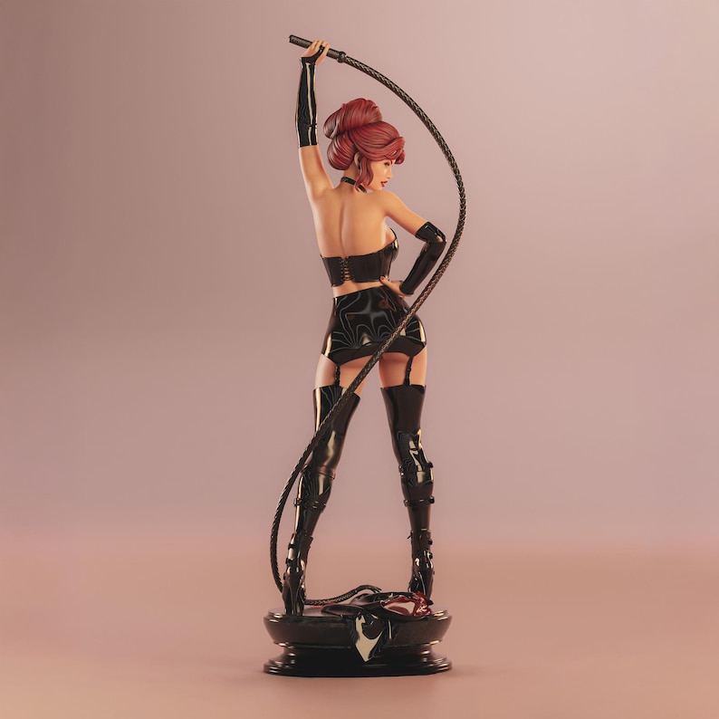 May include: A figurine of a woman in a black outfit, holding a whip. The figure has red hair and is posed with the whip raised. The base is black and round. The outfit includes a bustier, skirt, and thigh-high boots.