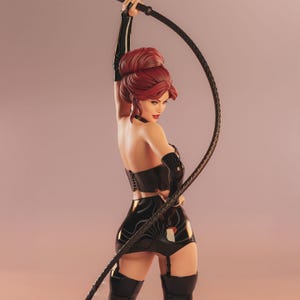 May include: A figurine of a woman with red hair, wearing a black corset, shorts, and boots, holding a black whip. The figure is posed against a soft pink background, with the whip arched overhead.