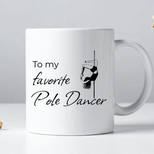 May include: White ceramic mug with a black graphic of a pole dancer and the text "To my favorite Pole Dancer". The mug has a curved handle and is suitable for hot or cold beverages. A gift for a pole dancing enthusiast.