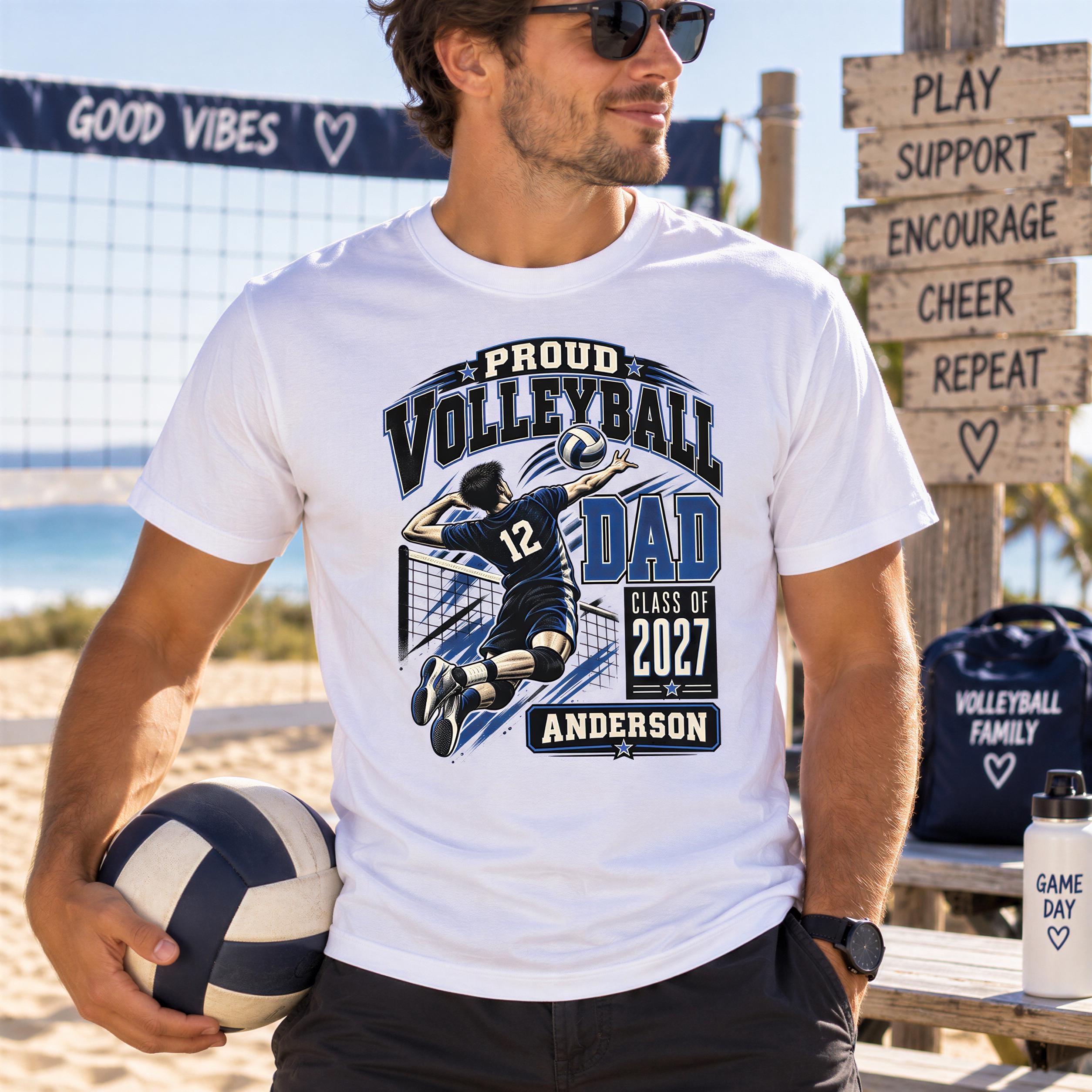 A man wearing a white t-shirt with a graphic of a volleyball player and text that says "Proud Volleyball Dad Class of 2027 Anderson" is standing on a beach.