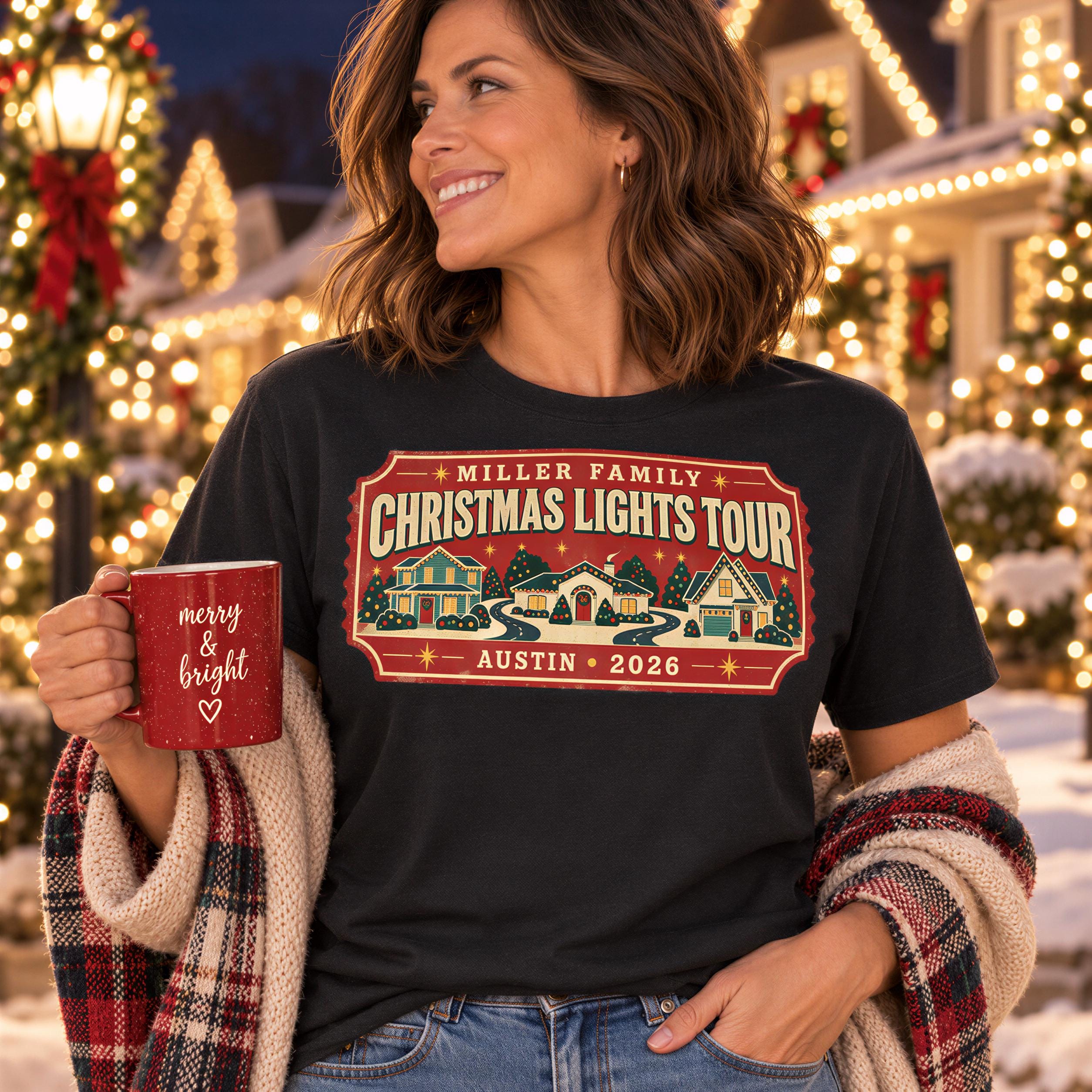 A woman wearing a black t-shirt with a Christmas lights tour design and holding a red mug with the text "merry bright" is smiling and standing in front of a festive background with Christmas lights.
