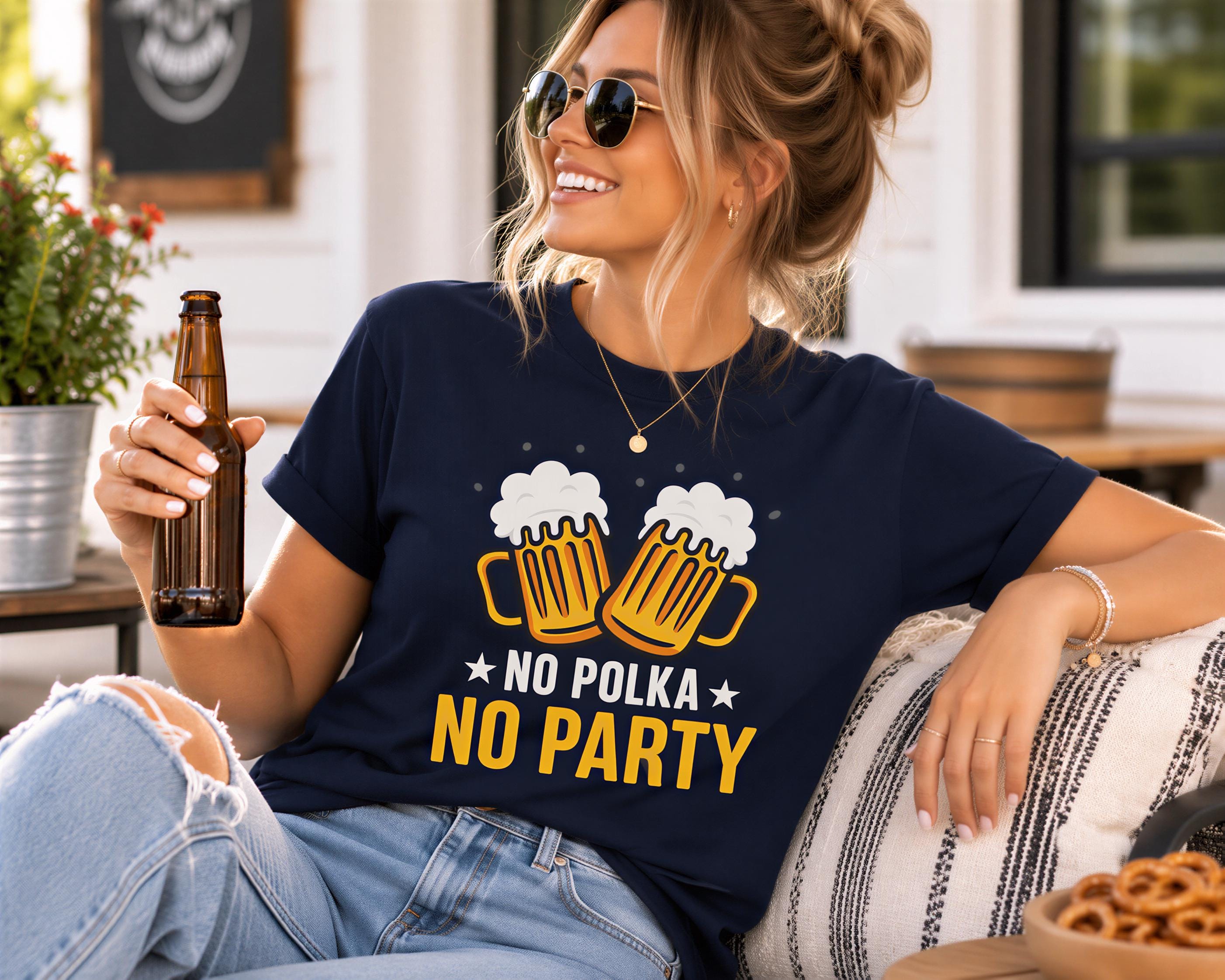 A woman wearing a blue t-shirt with a graphic design and holding a brown beer bottle, smiling and sitting outdoors.