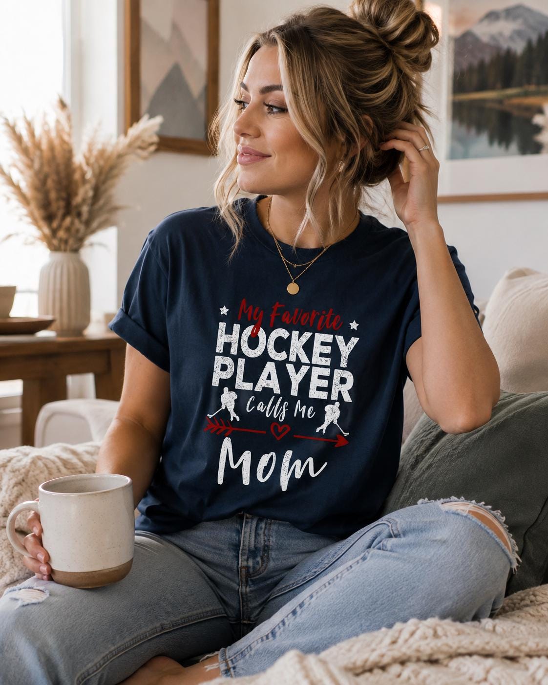 A woman wearing a navy blue t-shirt with text that says "My Favorite HOCKEY PLAYER calls me Mom" is sitting on a couch with a coffee mug in front of her.