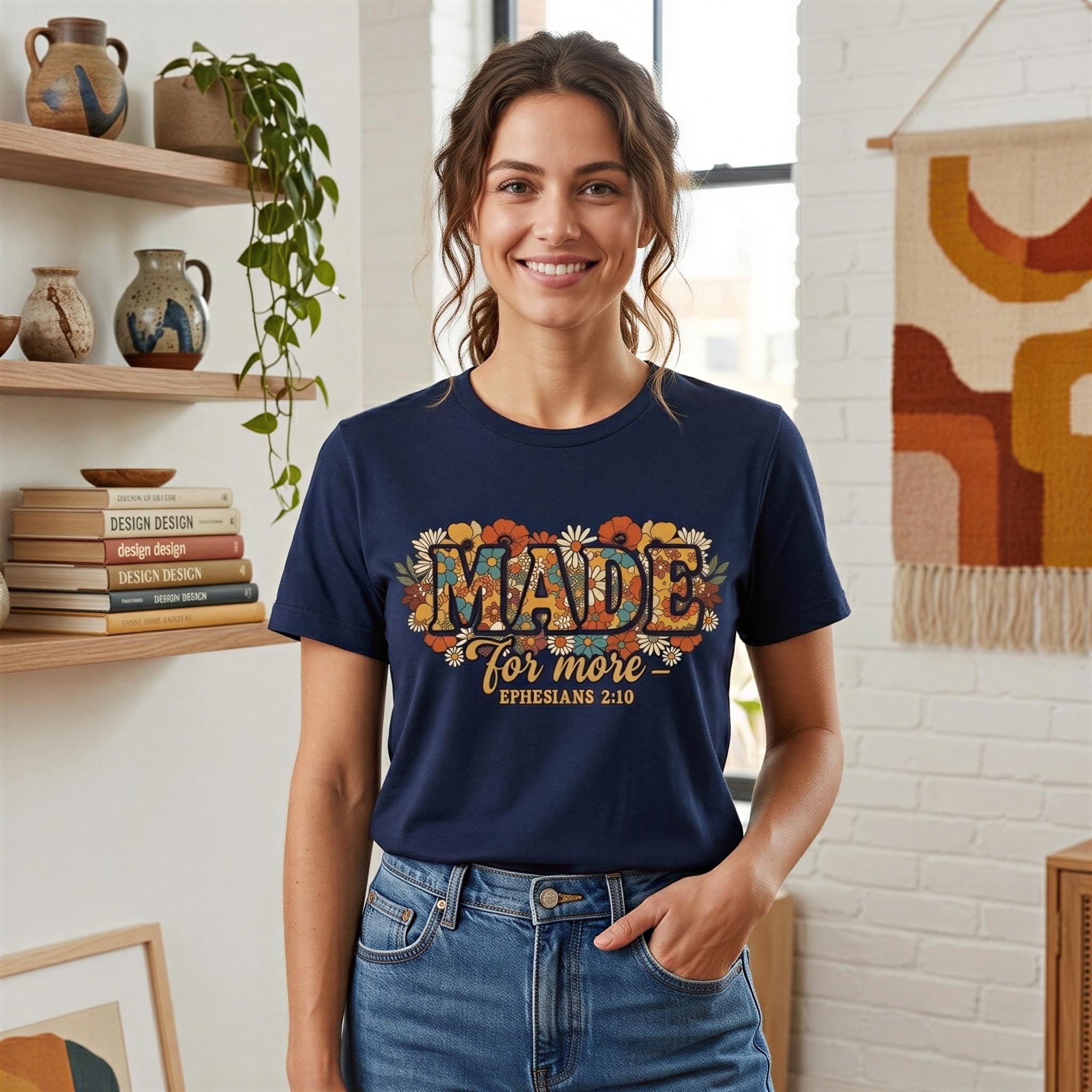 A woman wearing a navy blue t-shirt with a floral design and the text "MADE for more" stands in a room with shelves displaying various items, including books and vases.