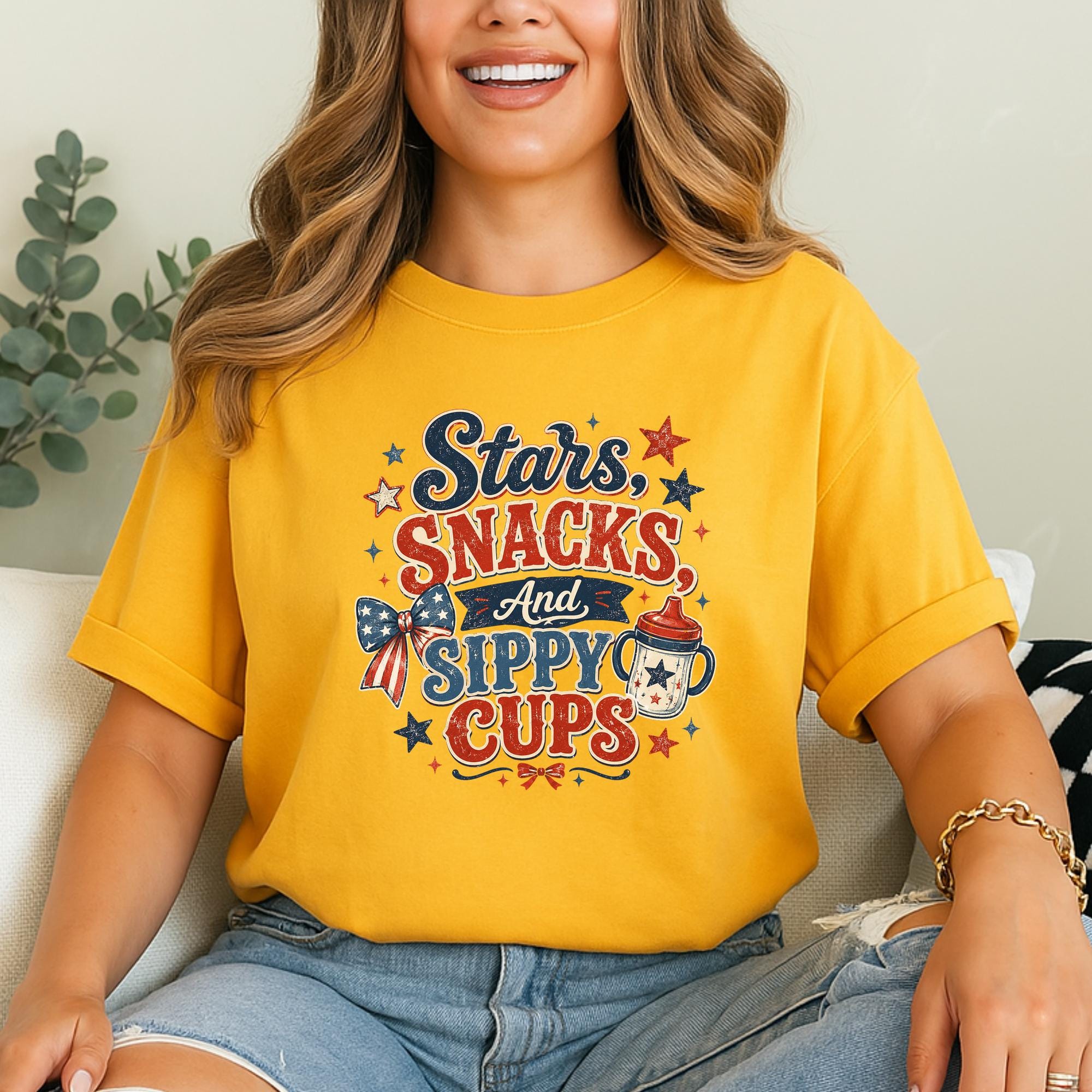A woman wearing a yellow t-shirt with a colorful graphic design that says "Stars. Snacks. And. Sippy cups"