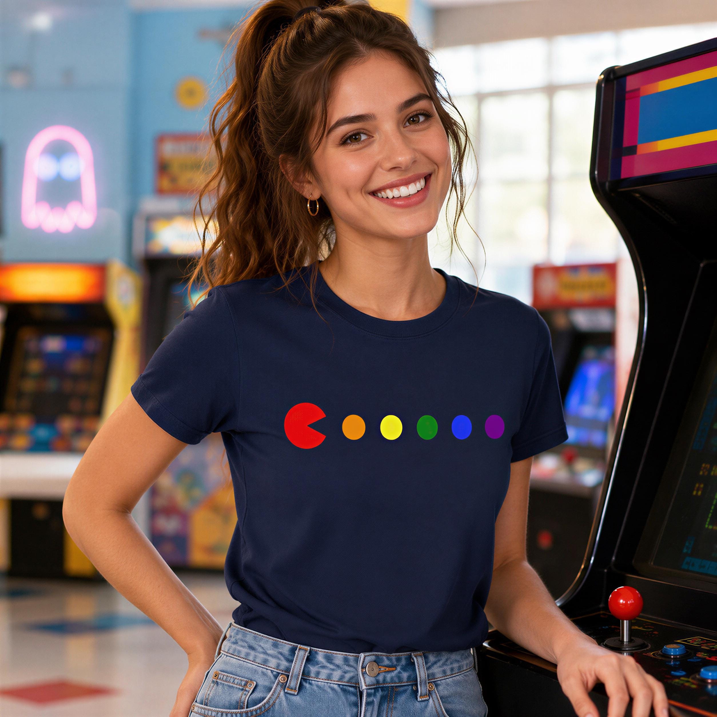 A smiling woman wearing a blue t-shirt with a colorful circle design stands in front of an arcade game.