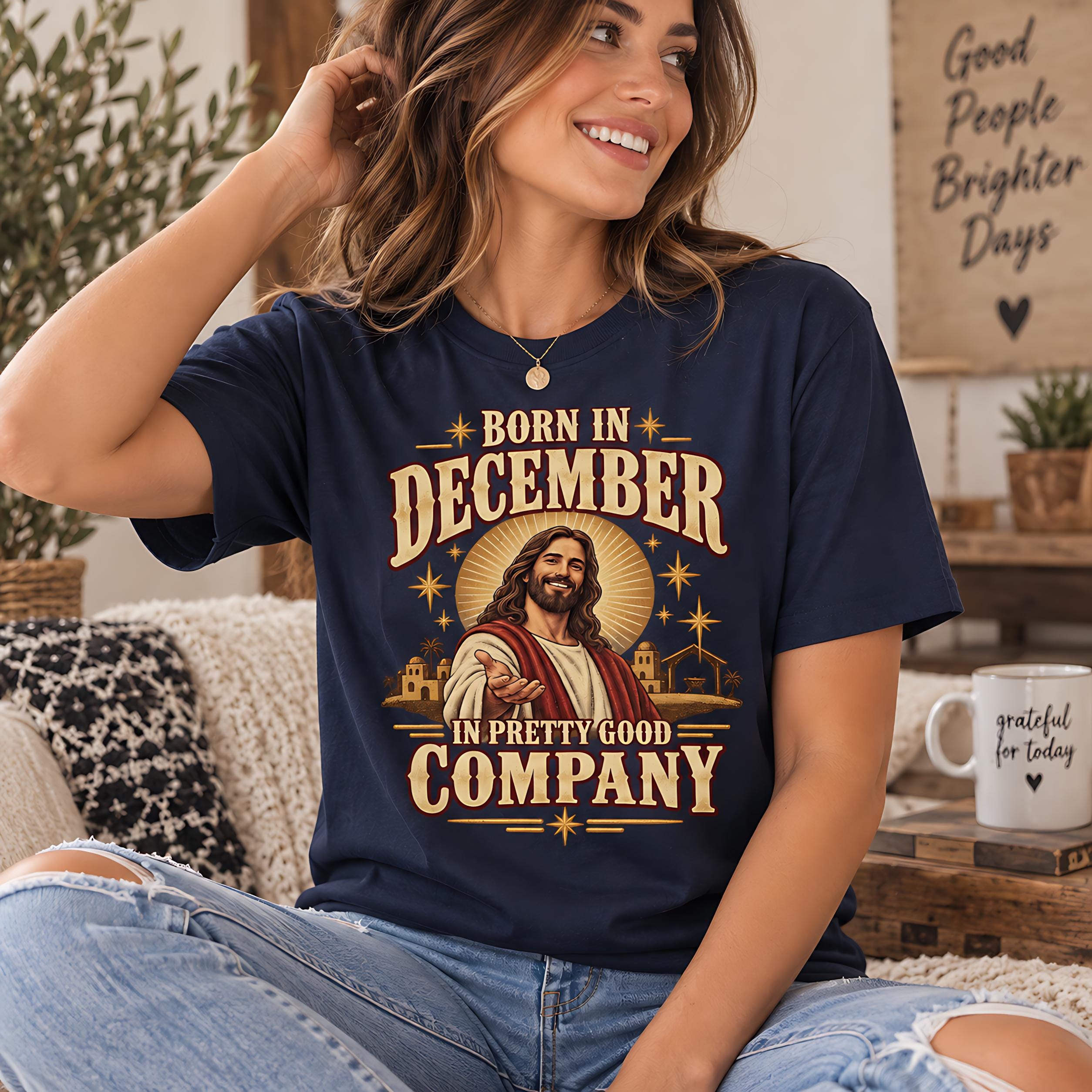 A woman wearing a navy blue t-shirt with a graphic design of a man and the text "Born in December in pretty good company" is sitting on a couch.