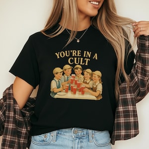 A woman wearing a black t-shirt with a graphic design of a group of people enjoying drinks together.
