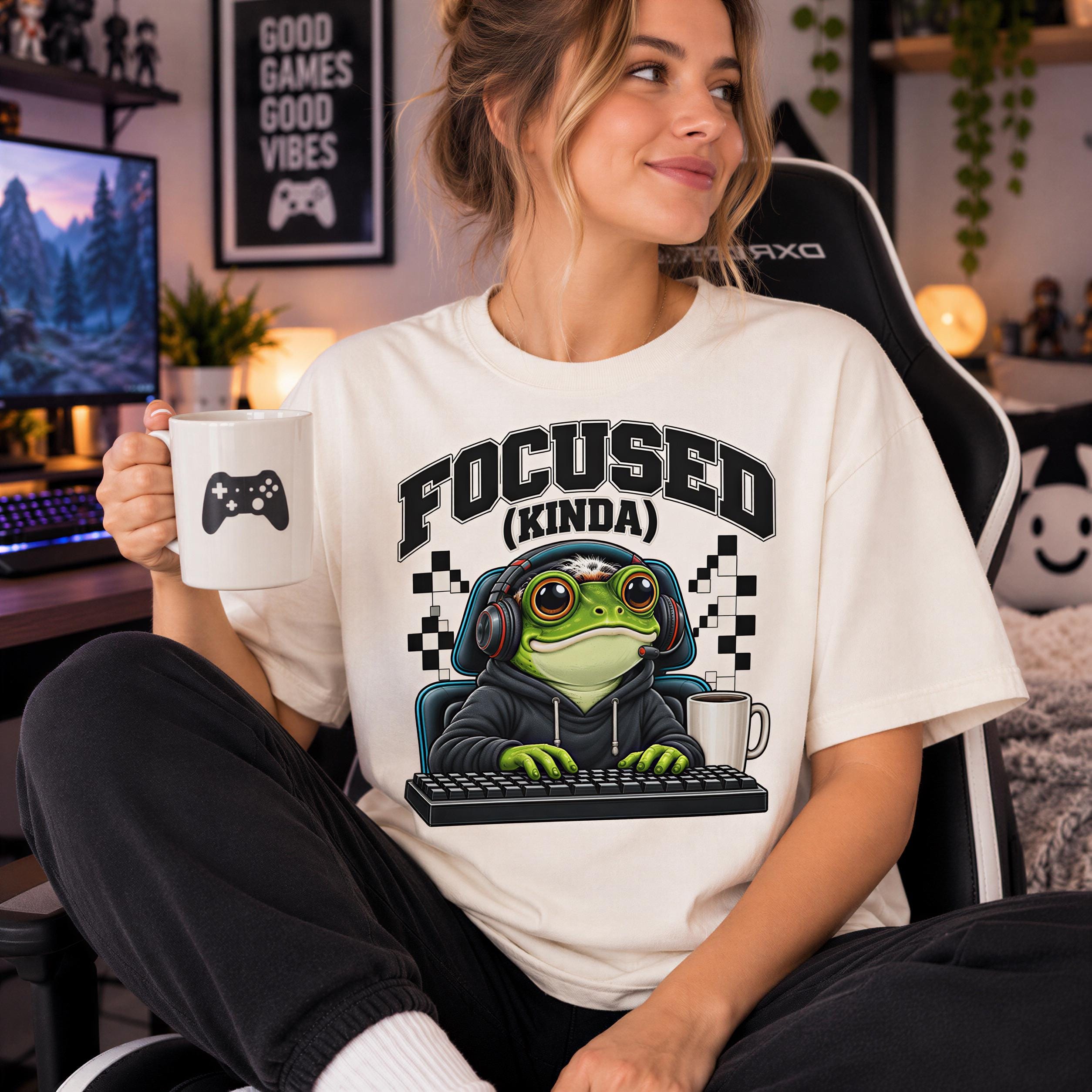 A woman sitting in a chair, wearing a white t-shirt with a graphic of a frog wearing headphones and holding a coffee mug.