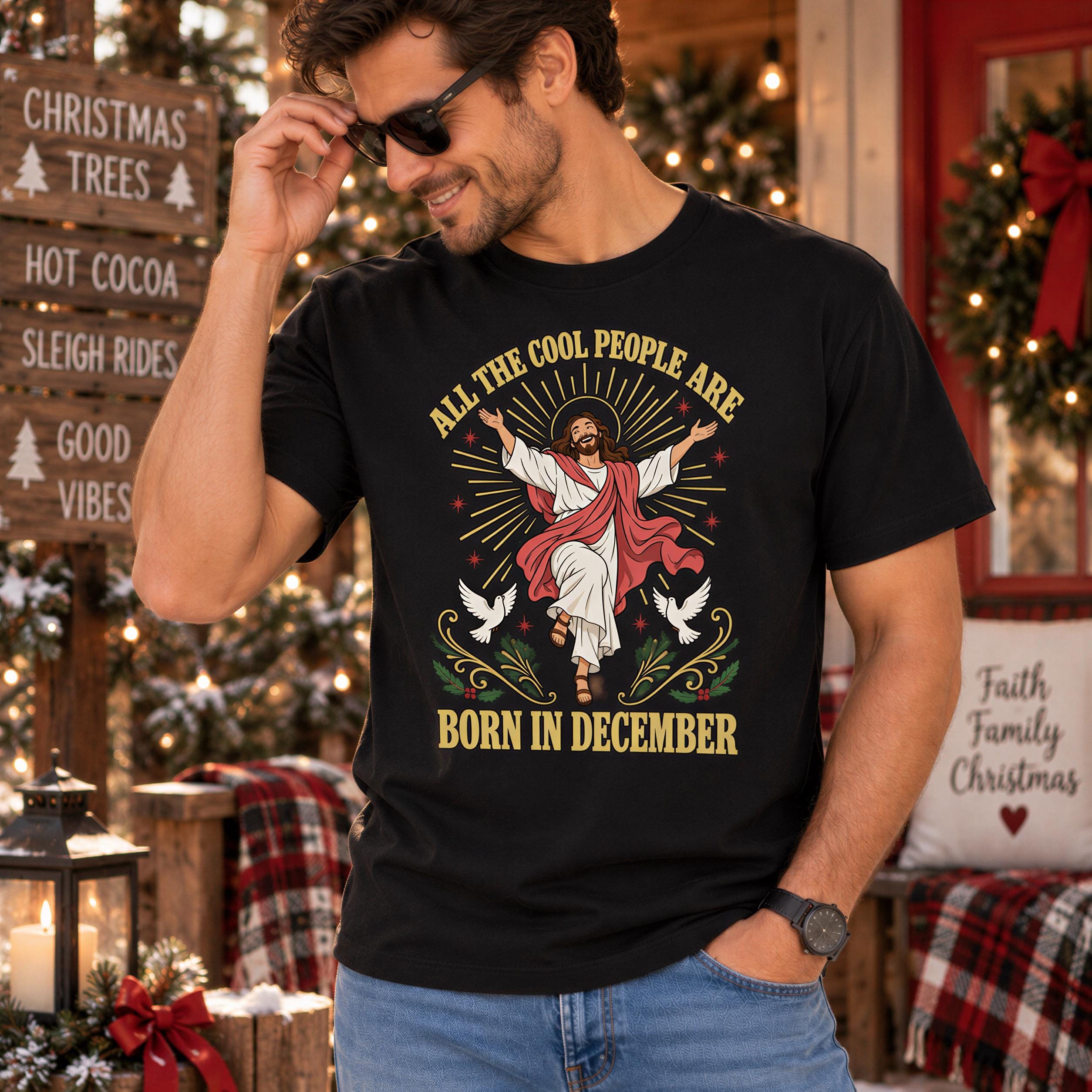 A man wearing a black t-shirt with a graphic design of Jesus Christ and the text "All the cool people are born in December" is standing in front of a Christmas tree and other holiday decorations.