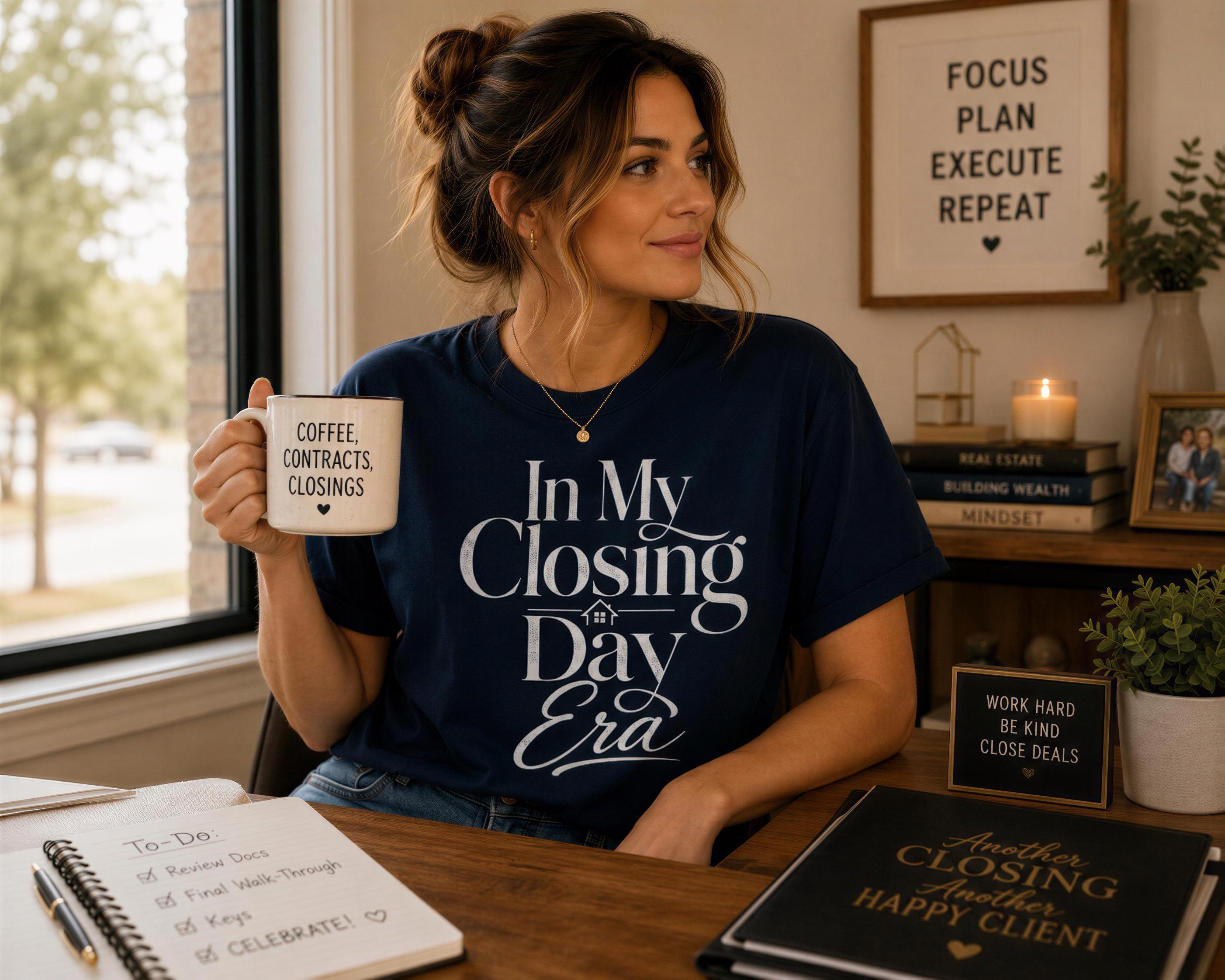 A woman wearing a navy blue t-shirt with the text "In My Closing Day Era" is sitting at a desk, holding a coffee mug and smiling. The desk has a notebook, a candle, and some books.