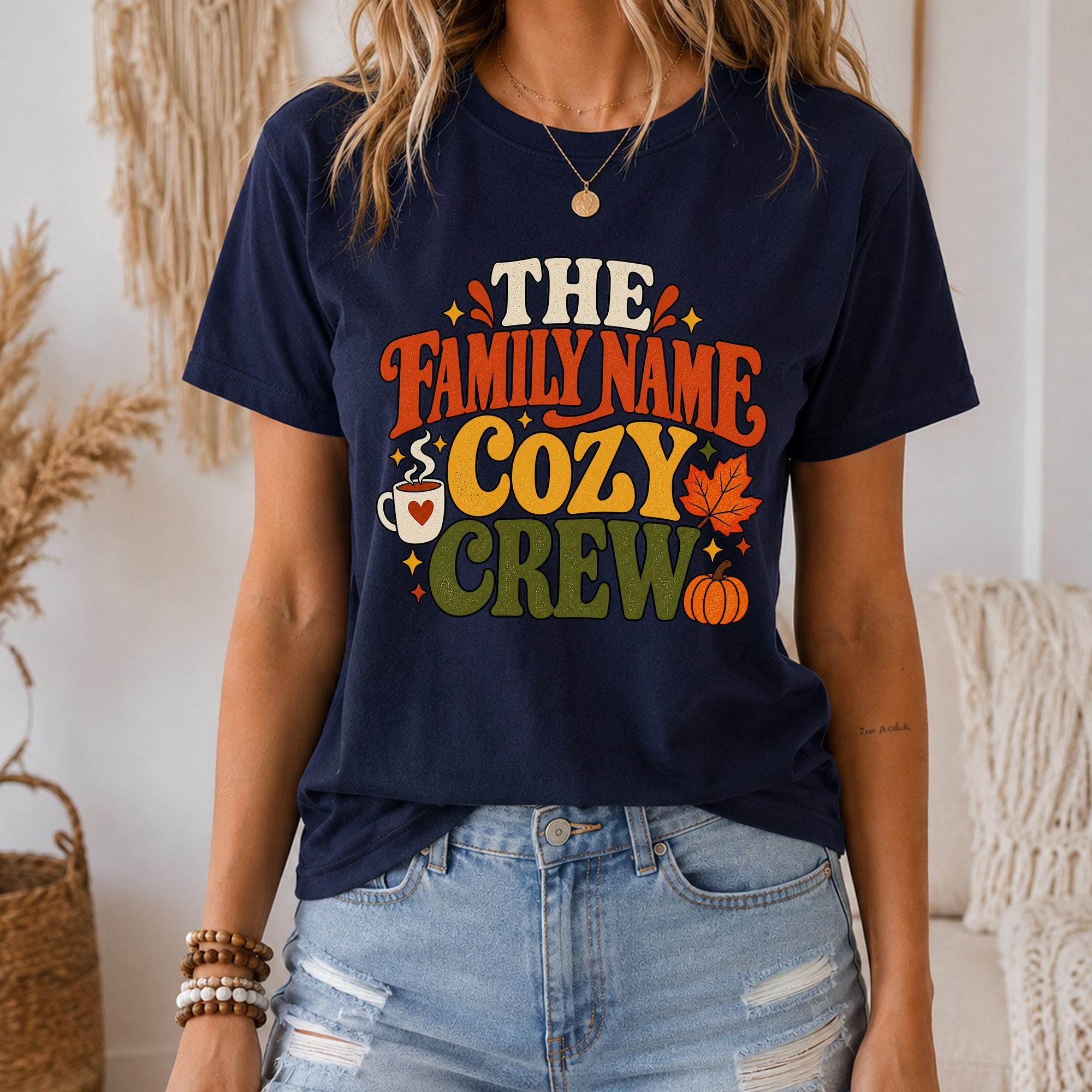 A woman wearing a navy blue t-shirt with a colorful graphic design that says "The Family Name Cozy Crew".