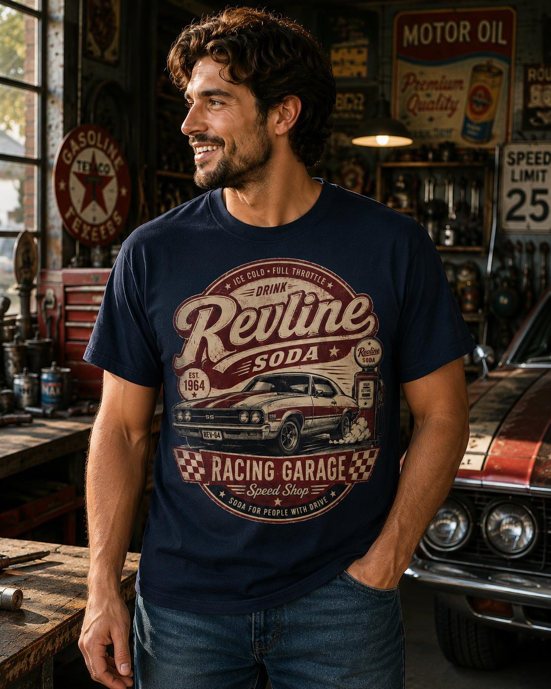 A man wearing a navy blue t-shirt with a vintage-style graphic of a car and a vintage-style graphic of a soda can, standing in a garage with various tools and equipment visible in the background.
