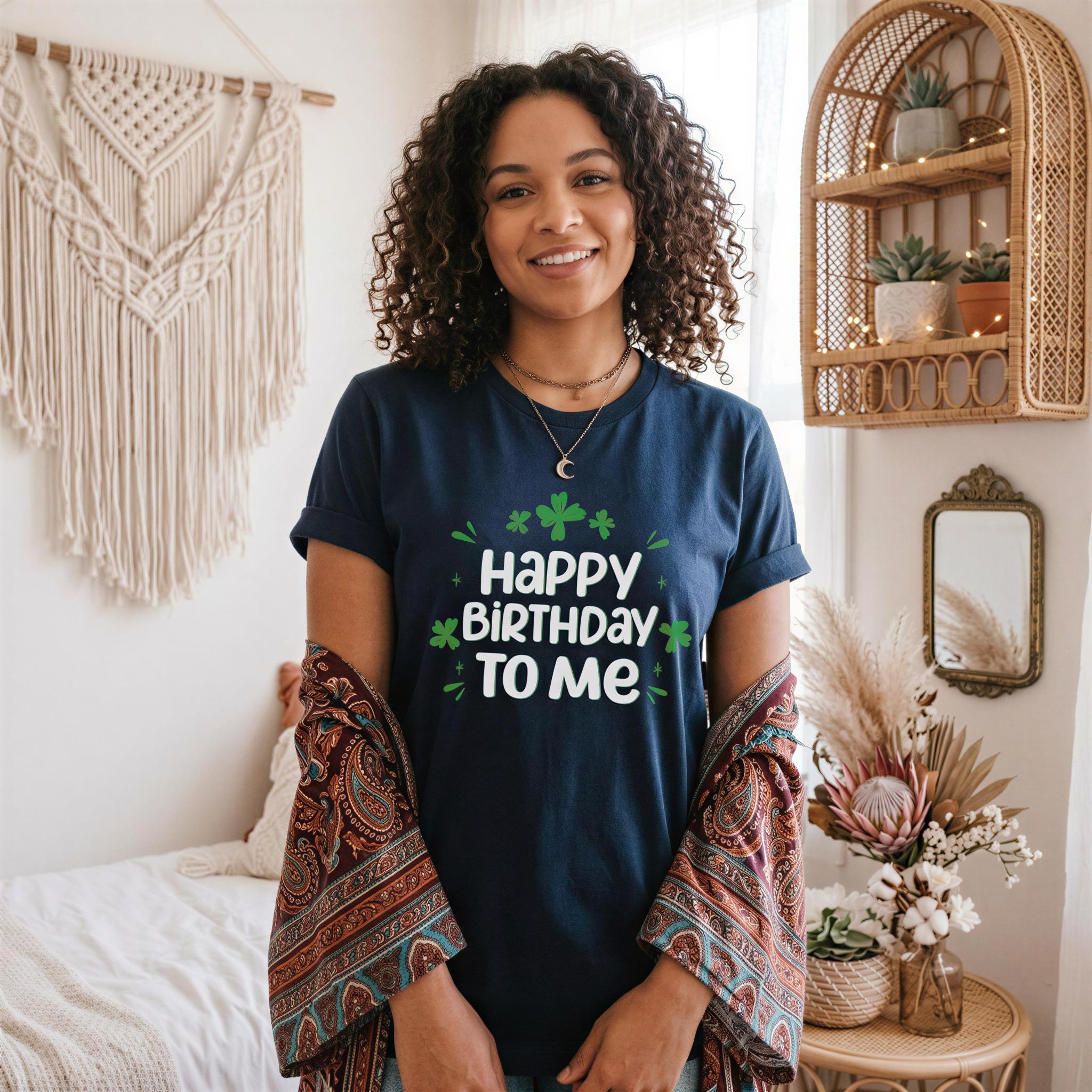 A woman with curly hair is standing in a room, wearing a blue t-shirt with the text "Happy Birthday to Me" printed on it. She is smiling and has a potted plant and a woven basket nearby.