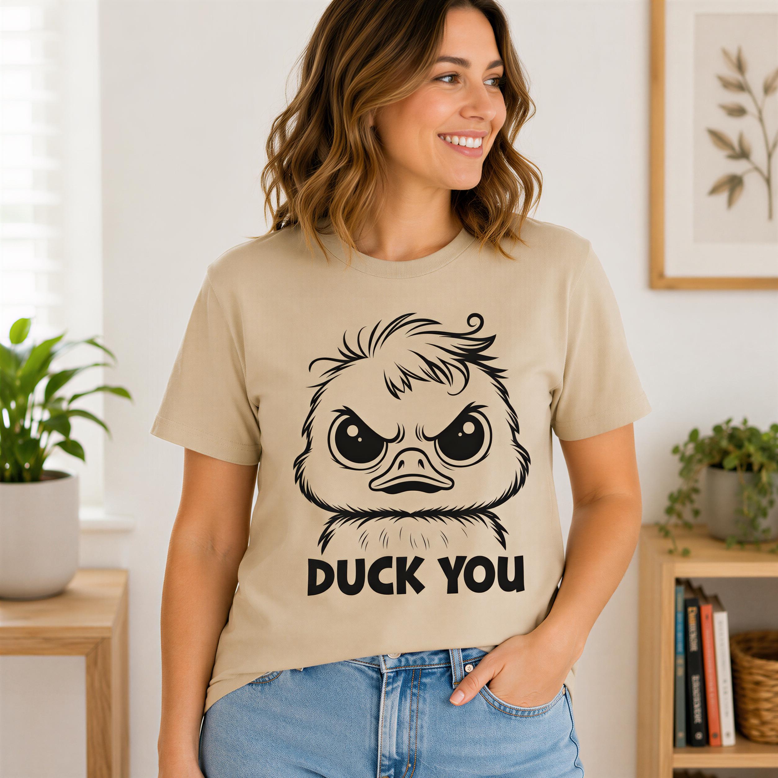 A woman wearing a beige t-shirt with a cartoon duck and the text "DUCK YOU" is smiling and posing in a room with a plant and bookshelf in the background.