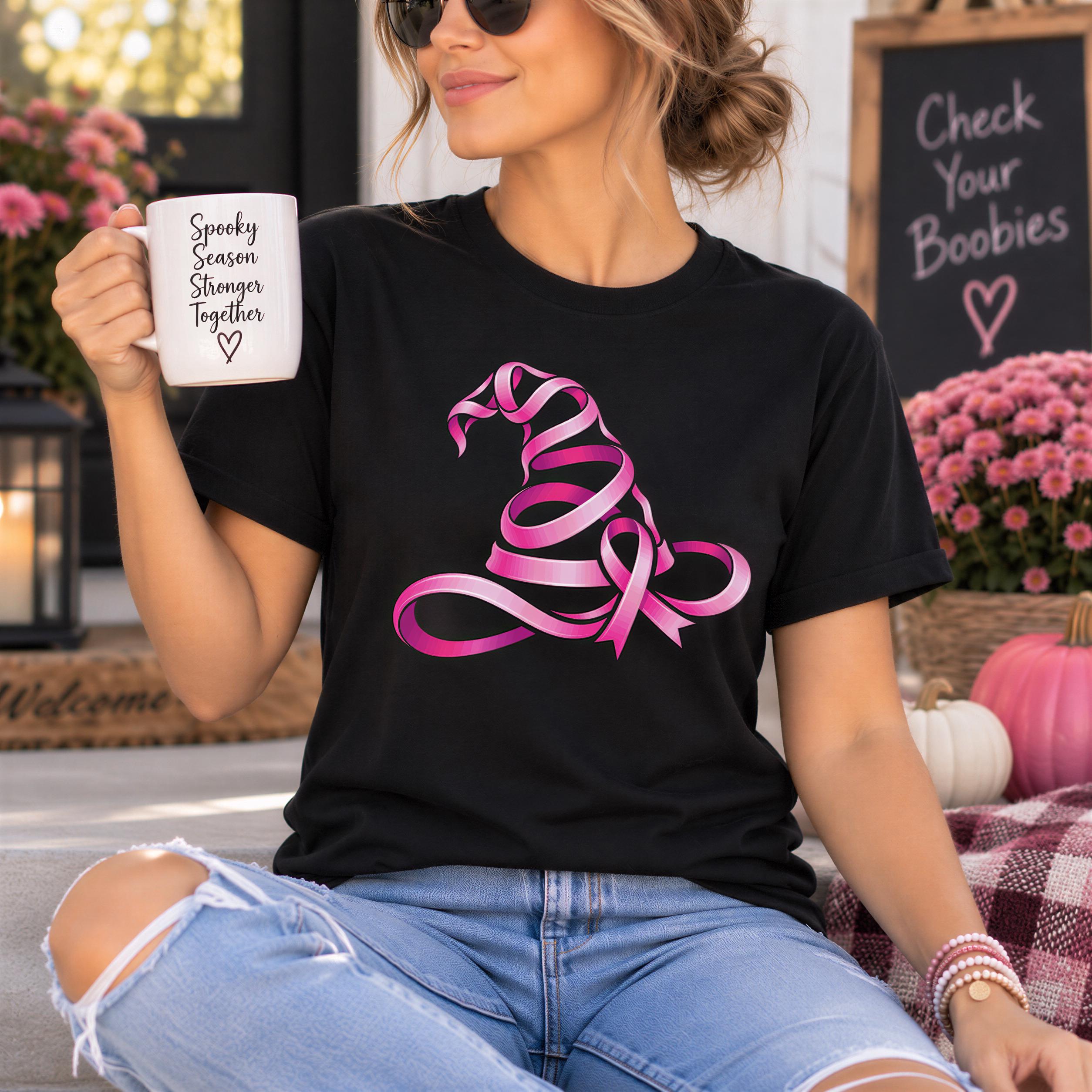 A woman wearing a black t-shirt with a pink ribbon design is sitting on a bench, holding a mug with the text "Spooky Season Together" printed on it.